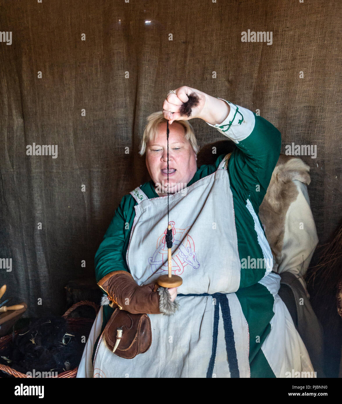 La donna re-enactor in abiti Viking includente un hangerock ricamato (grembiule gonna) dimostrando un mandrino di caduta durante il Largs Viking festival Foto Stock