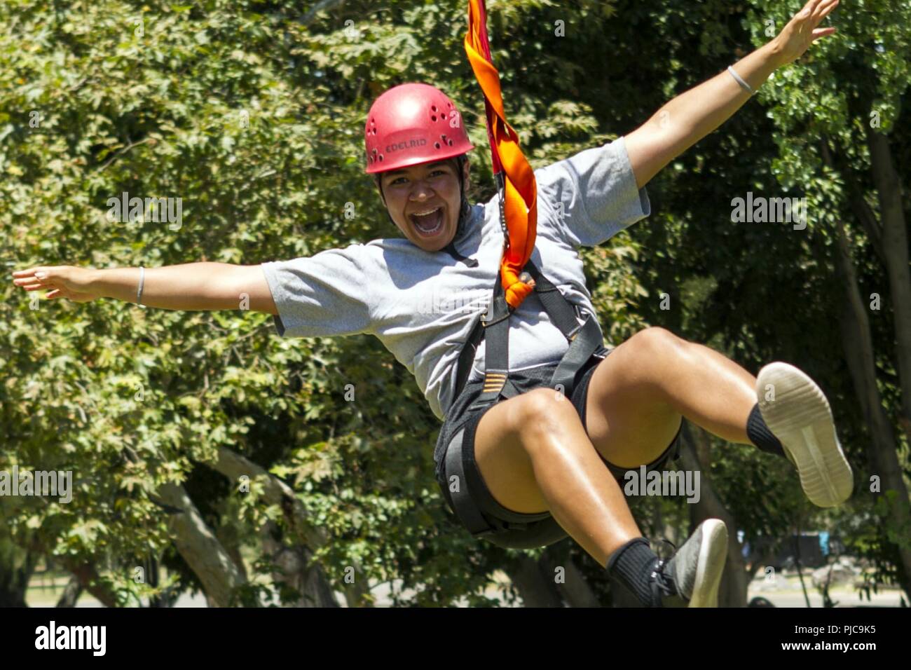 Sunburst sfida della gioventù Academy Classe 22 Logomua candidato Quiroga, del plotone Firehawks, ingrandisce in passato su mentre cavalcate zip line terminare verso il basso a partire da una fune tower, luglio 19, 2018 all'Orange County ropes course di Anaheim, in California. Le funi corso offre ai candidati la possibilità di spingere se stessi sia mentalmente e fisicamente, per costruire la fiducia e di iniziare a lavorare come un team mentre è ancora in fase di acclimatazione della sfida del programma. Foto Stock