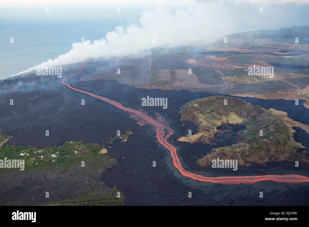 La lava eruttata dal fessura 8 di Hawaii vulcano Kilauea est Zona di rift scorre come un fiume incandescente attorno a Montagna Verde cono di scorie per inserire l'oceano. Foto Stock