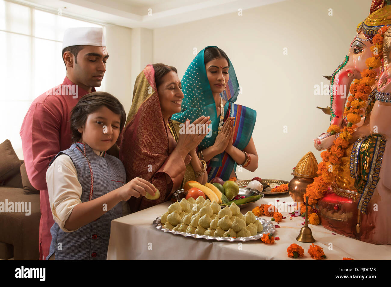La famiglia che prega sulla Ganesh Chaturthi mani di piegatura in cui il bambino winks e prende un modak dal prasad Foto Stock