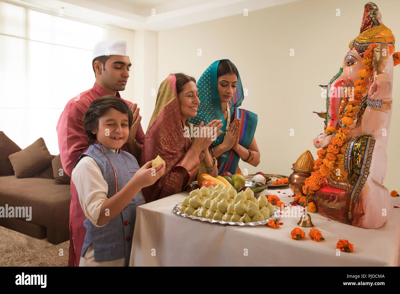 La famiglia che prega sulla Ganesh Chaturthi mani di piegatura in cui il bambino winks e prende un modak dal prasad Foto Stock