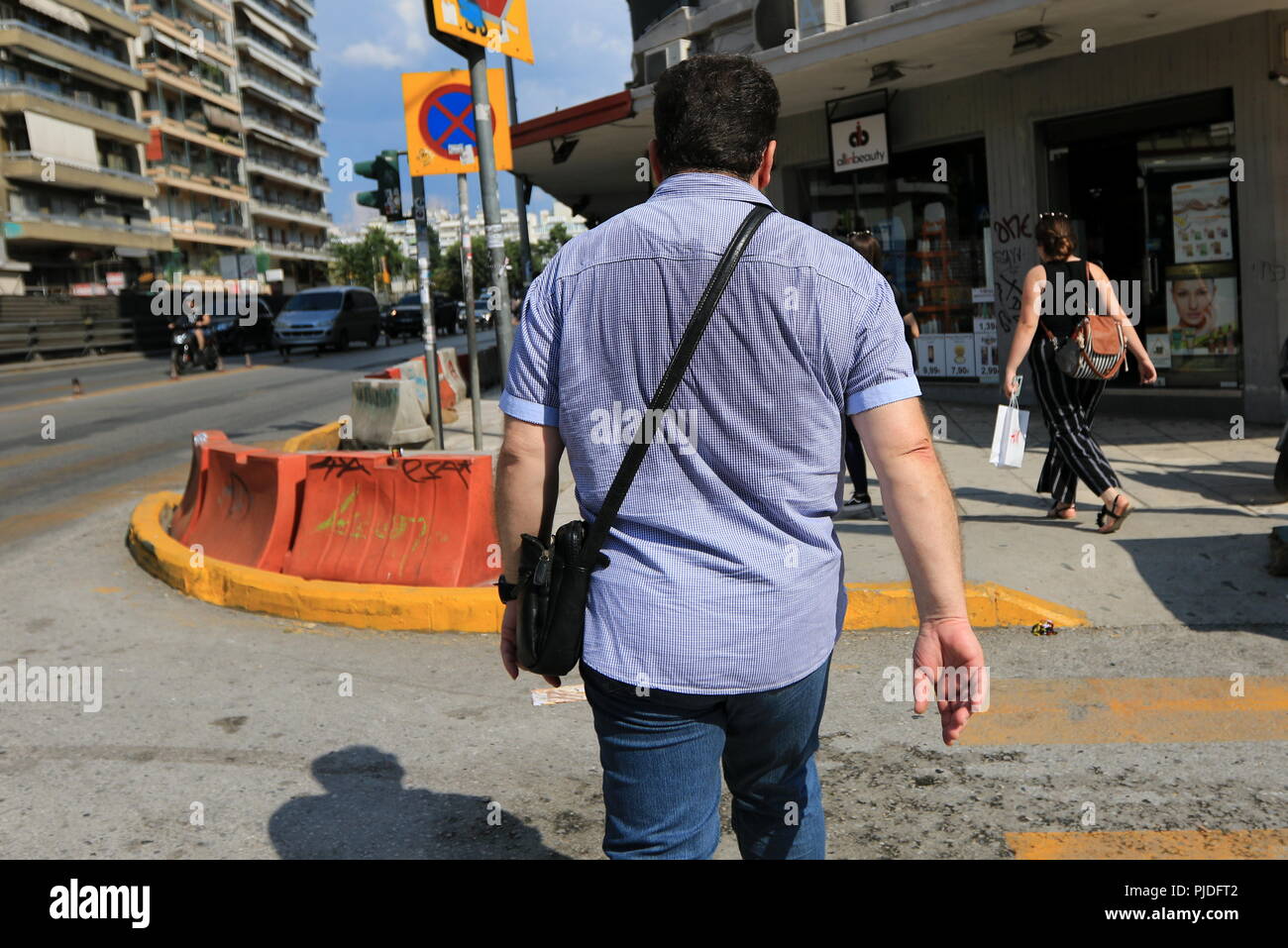 Uomo che cammina sulla strada con il retro della sua maglietta imbevuto di sudore Foto Stock