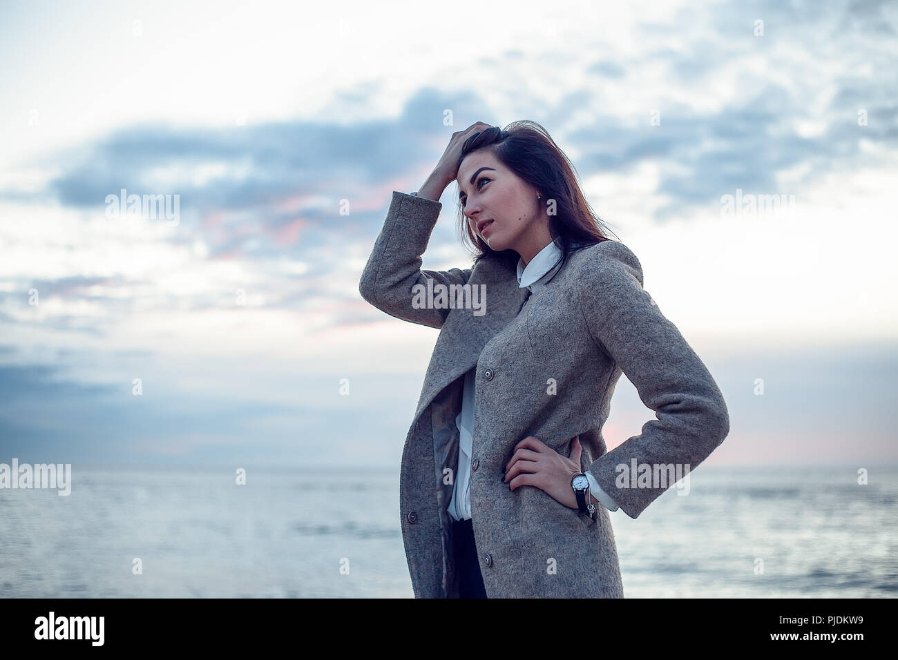 Giovane donna in piedi sulla spiaggia, mano mantenendo i capelli dal viso, espressione pensosa Foto Stock