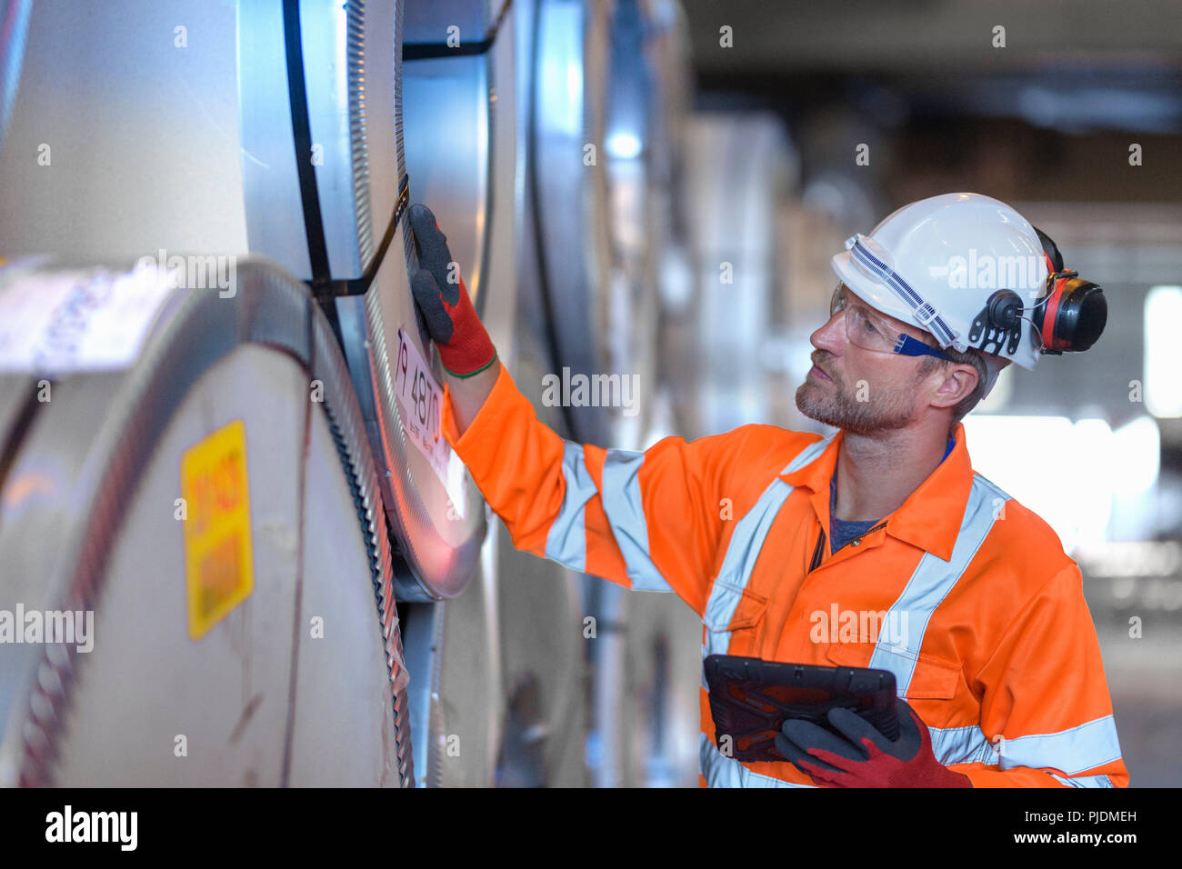 Lavoratore con tavoletta digitale per ispezionare le righe del foglio di acciaio in deposito a porto Foto Stock