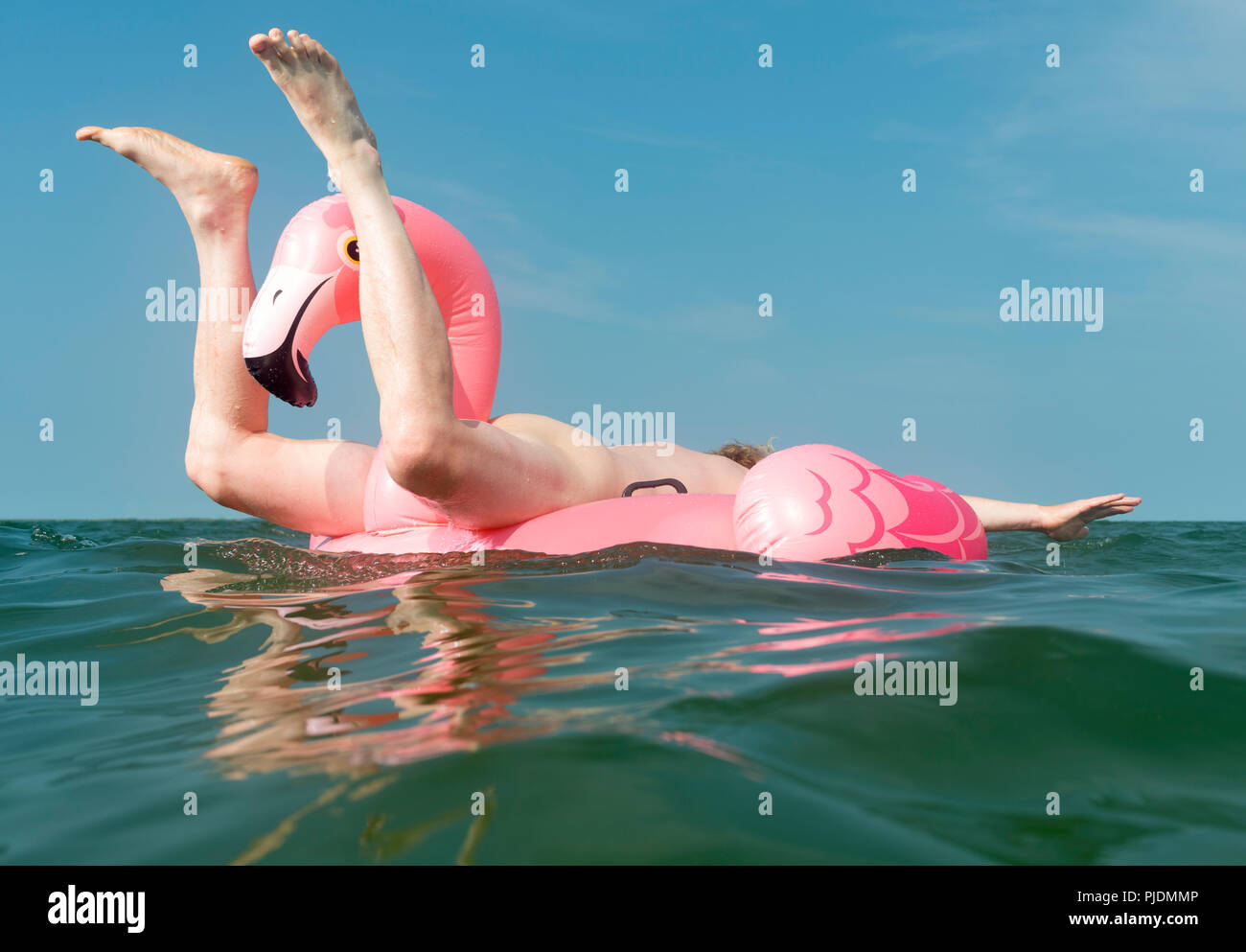 Luomo nudo giocando sulla flamingo gonfiabile in mare Foto Stock