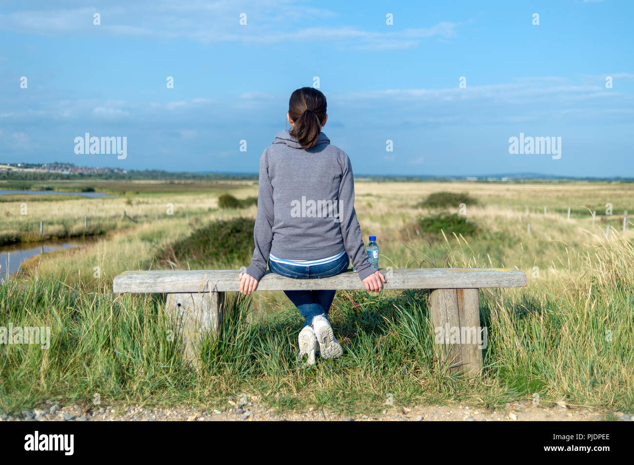 Vista posteriore di una donna seduta su una panca in legno guardando la campagna. Foto Stock