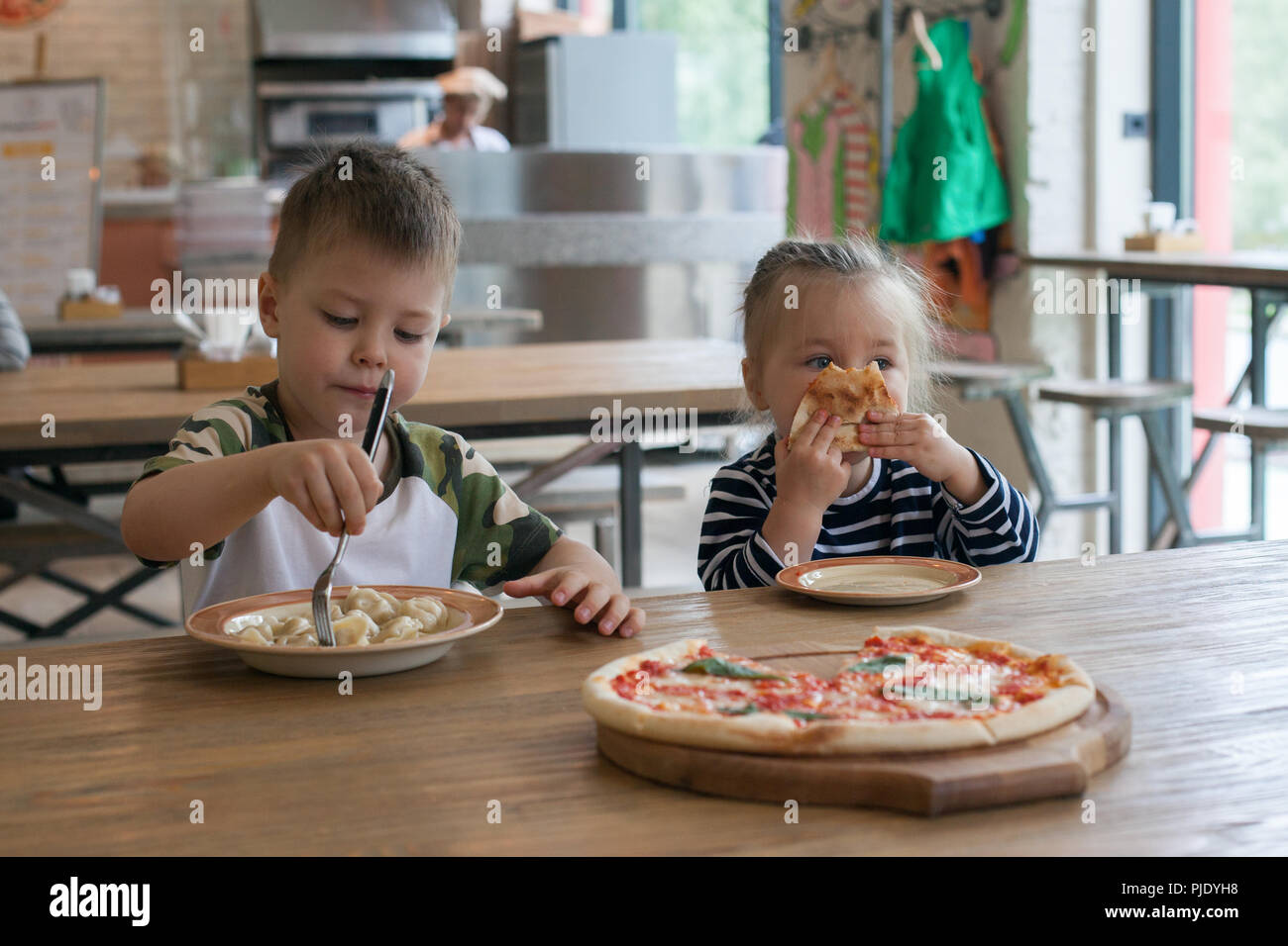 I bambini mangiano la pizza e carne gnocchi al cafe. I bambini a mangiare cibo malsano in ambienti chiusi. Fratelli in cafe, vacanza famiglia concetto. Foto Stock