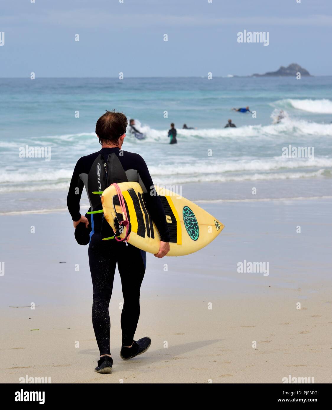 Un uomo che porta una tavola da surf a camminare verso il mare,Sennen Cove,Cornwall,l'Inghilterra,UK Foto Stock