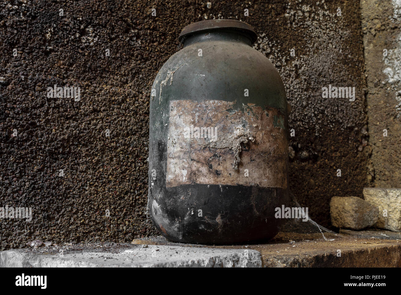 Molto vecchio e nero invecchiati jar coperto di polvere e spider web in piedi di fronte ad un muro di cemento a basamento Foto Stock