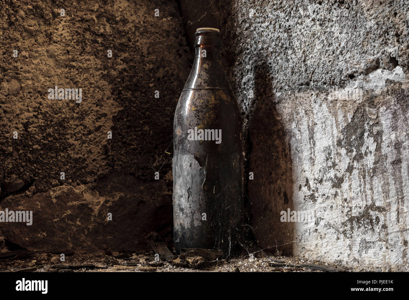 Molto vecchio e invecchiato bottiglia marrone coperto di polvere e spider web in piedi di fronte ad un muro di cemento a basamento Foto Stock