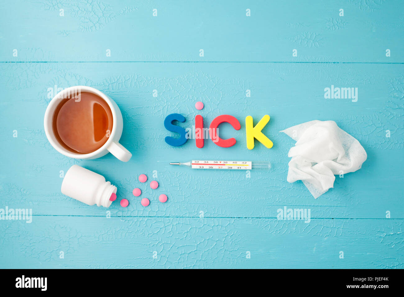 Su uno sfondo blu un termometro, compresse, un tovagliolo stropicciato un iscrizione malati e tè Foto Stock