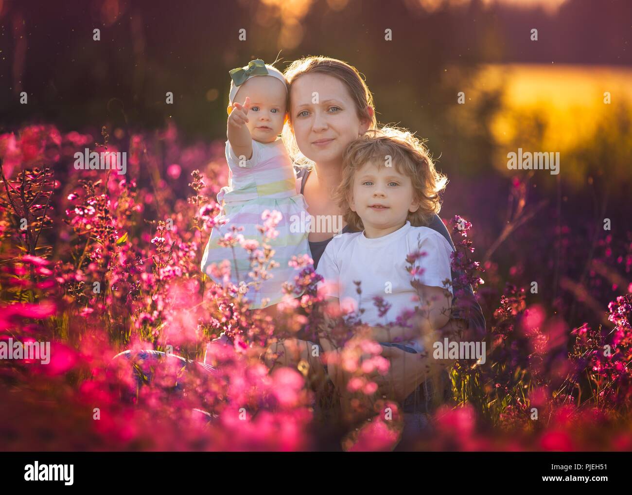 Madre e figlio e figlia in seduta a fiori di colore rosso. Ritratto di famiglia. Foto Stock