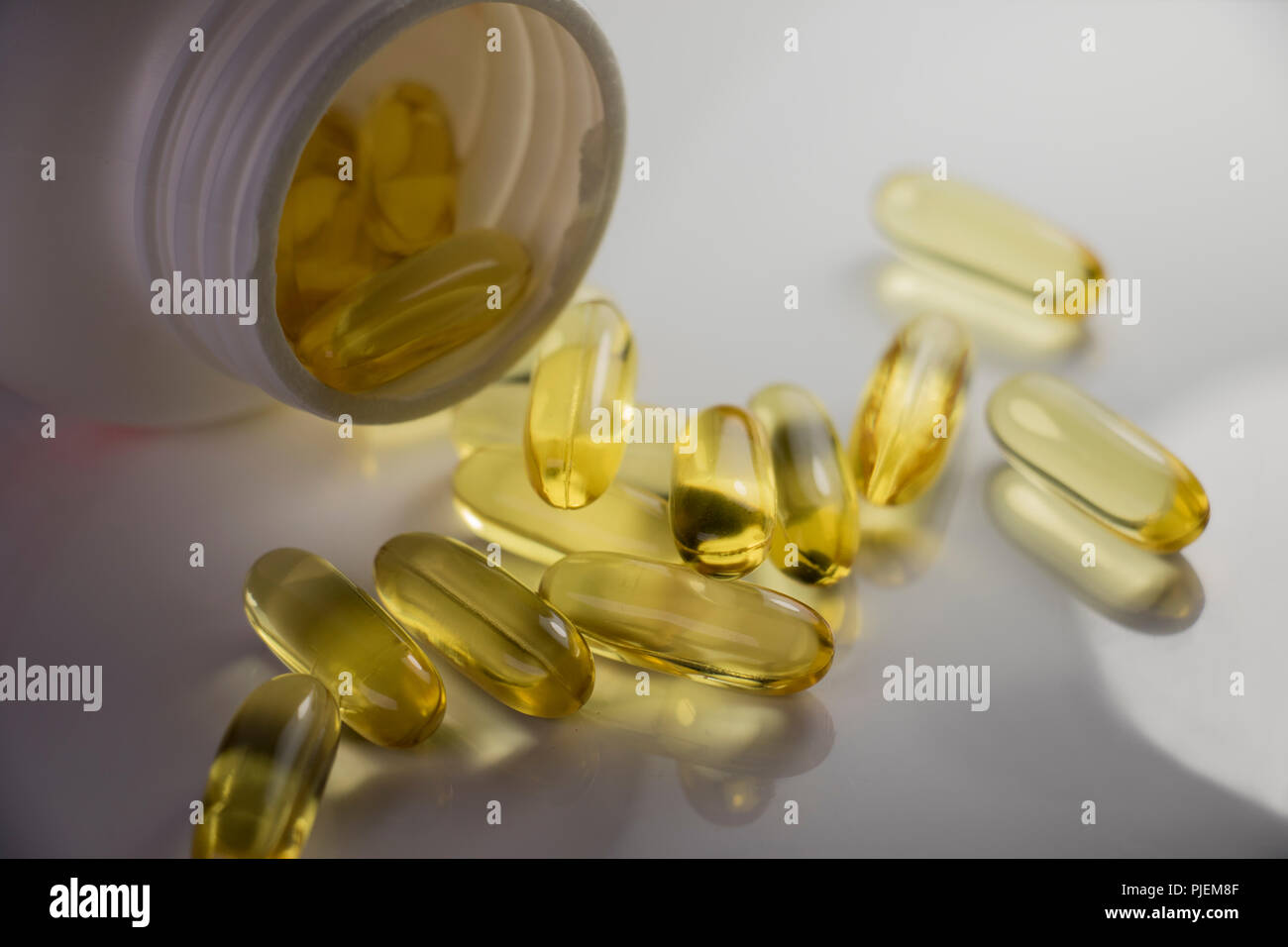 Omega 3 olio di pesce. Le capsule di chiara la fuoriuscita di un open  vitamina contenitore su di una superficie bianca.drug store Foto stock -  Alamy