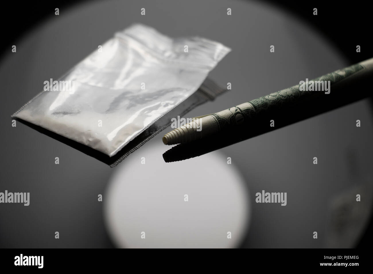 Close up di un sacco di droghe e una carta arrotolata bill su un nero riflettente tabella. il consumo di droghe illecite in aumento. Foto Stock