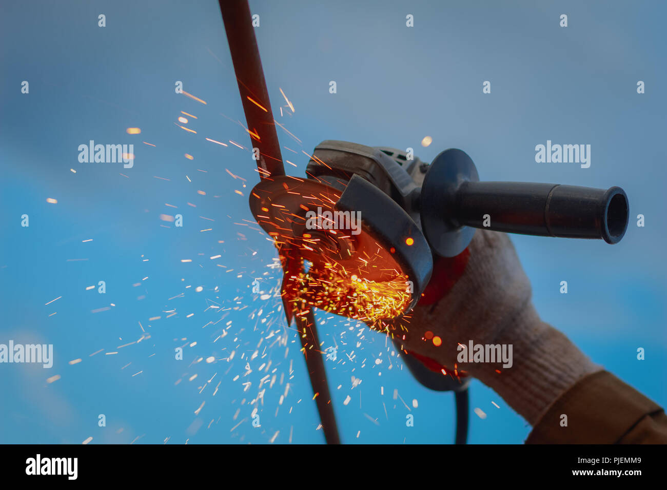 Mola in lavorazione a mano con scintille quando si lavora con metalli su uno sfondo blu Foto Stock