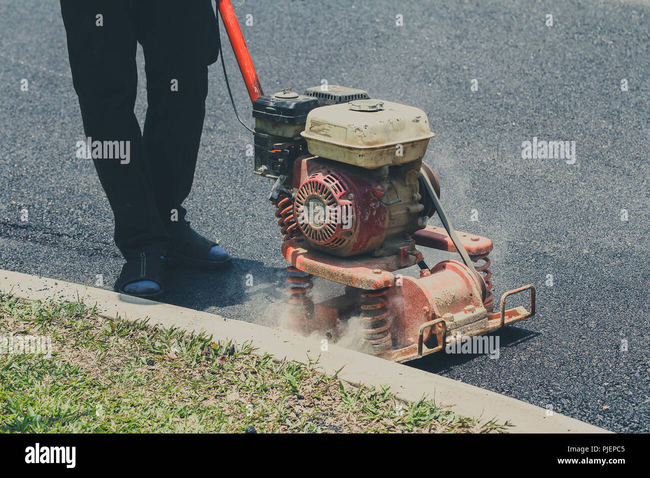 Lavoratore utilizza la piastra vibrante compattatore di asfalto di compattazione a riparazione su strada Foto Stock
