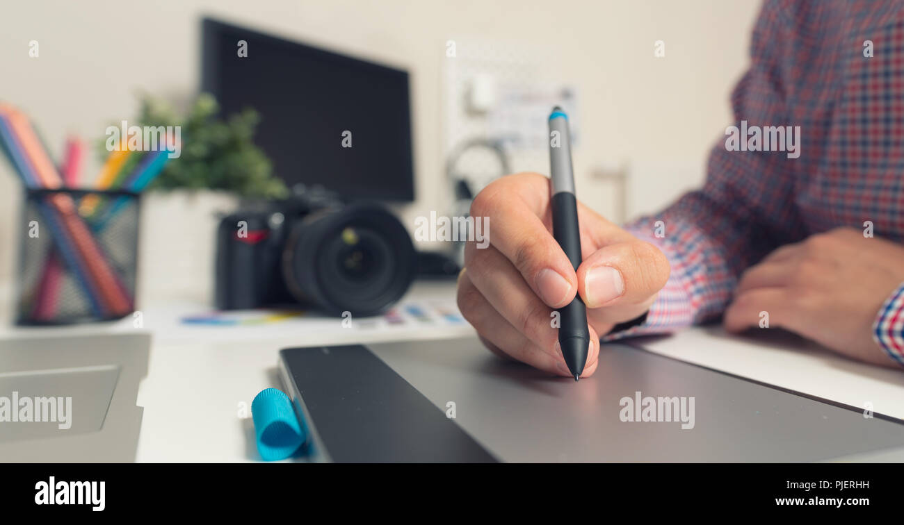 Graphic designer che lavora sulla tavoletta digitale. Fotocamera sulla scrivania in background. Fotografo lavorando in ufficio. Foto Stock