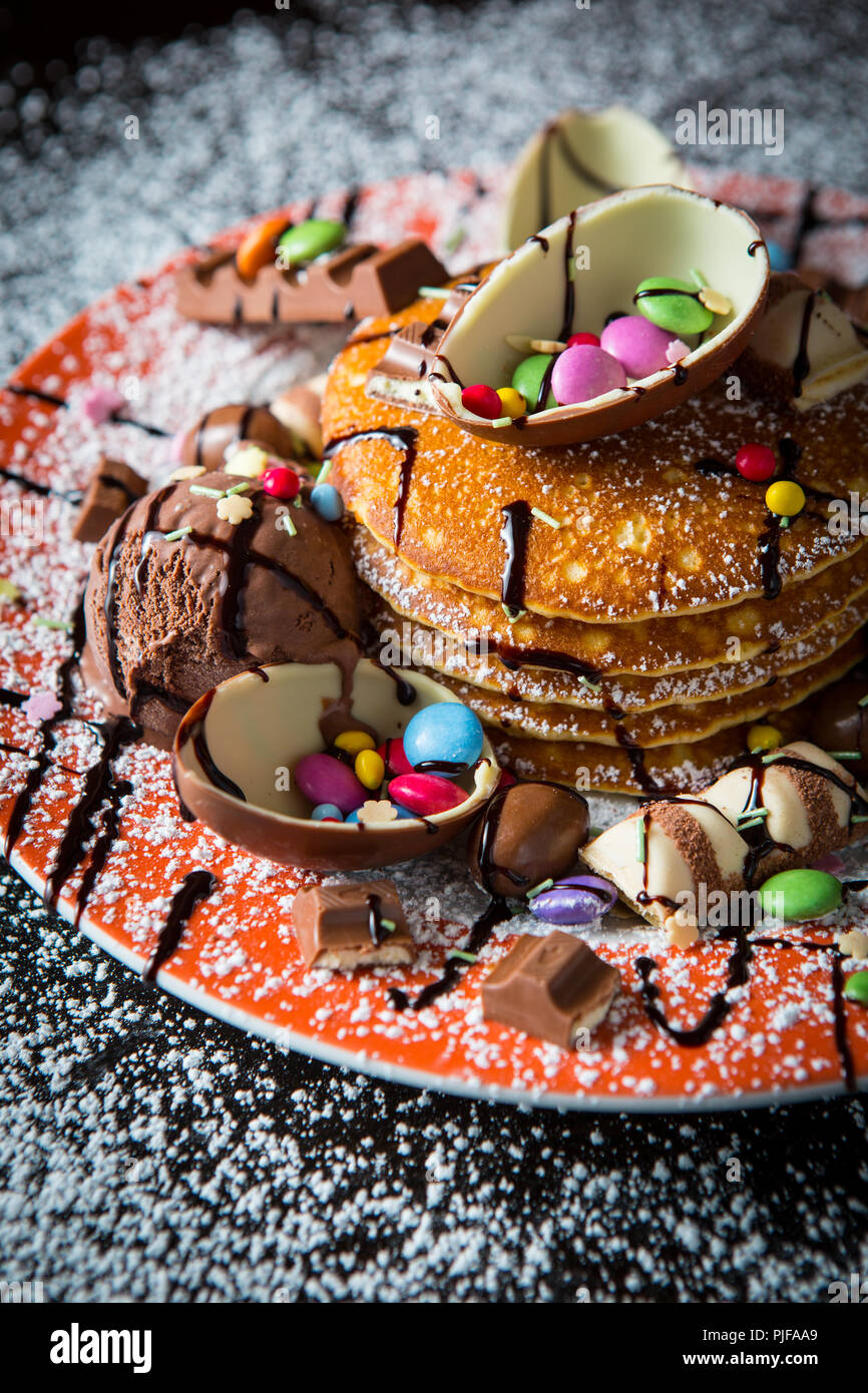 Una pila di cucinato al momento American toffee frittelle una spruzzata di sciroppo al cioccolato e guarnita con dimezzato di uova di cioccolato, dolci cioccolatini all'ora Foto Stock