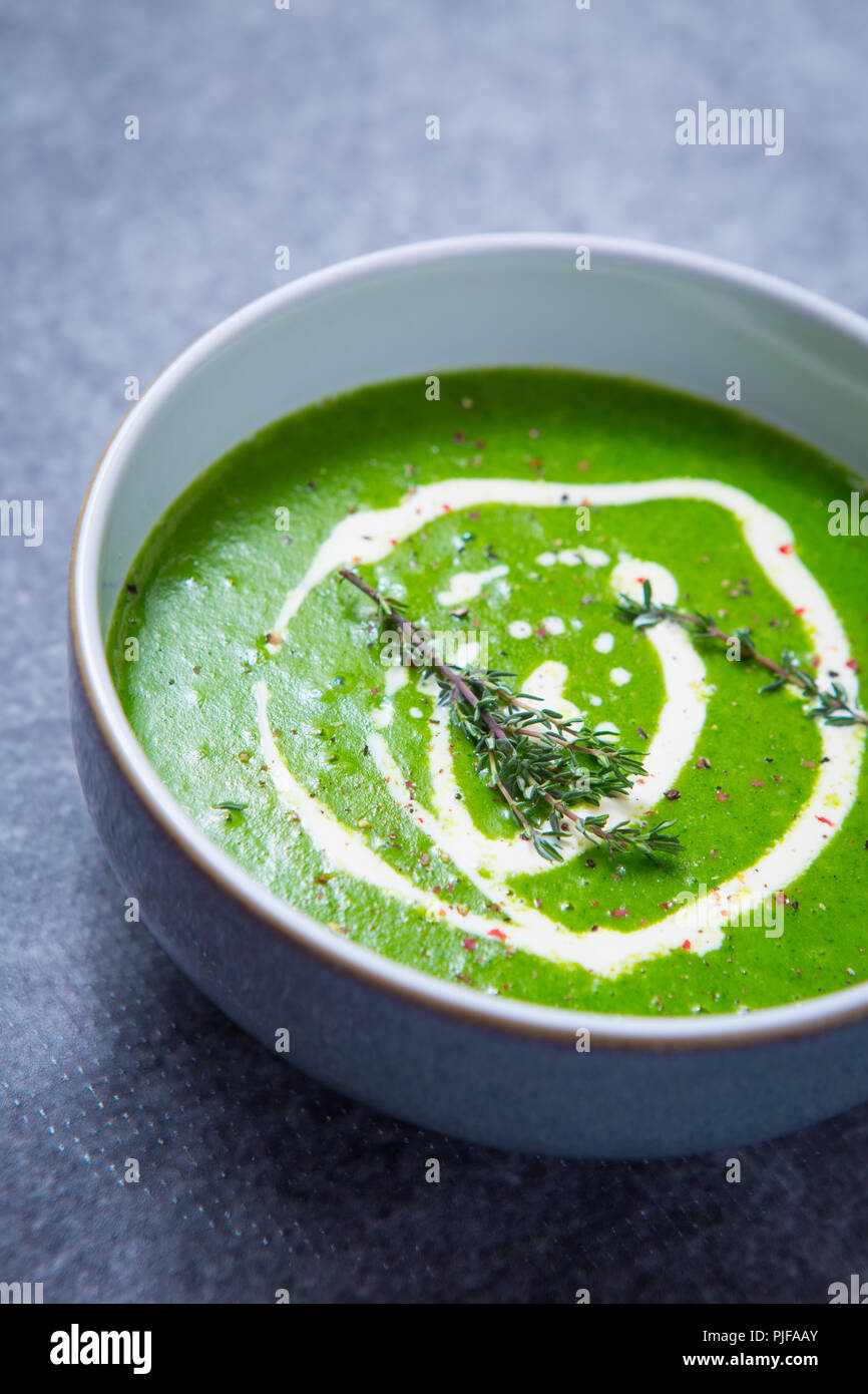 Colore verde brillante di crescione zuppa con una pioggerellina di doppia panna, guarnita con fresco rametti di timo e una macinatina di pepe e sale, su sfondo grigio Foto Stock