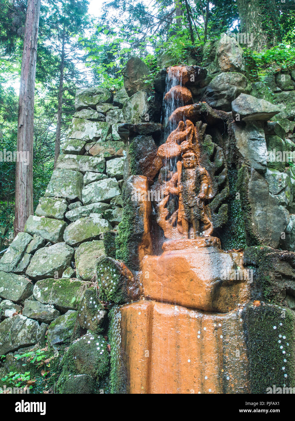 Myoo Fudoo statua, in cascata, onrange macchiata dalla sorgente di acqua minerale, offerte di moneta attaccata alla Moss, Maegamiji, tempio 64, Shikoku 8 Foto Stock