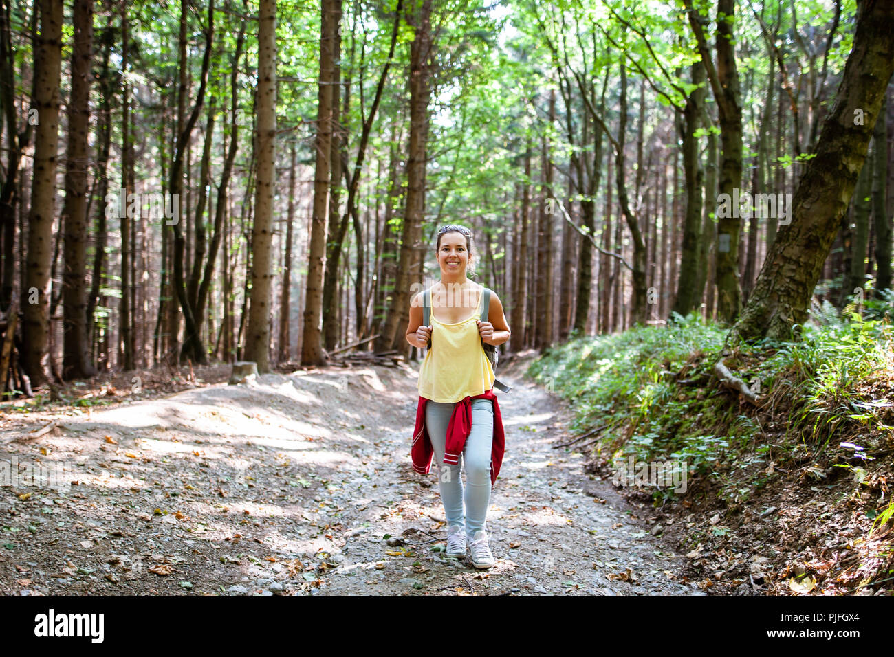 Bella donna sorridente nel percorso in una foresta durante le escursioni su una collina durante il Sunrise in estate Foto Stock