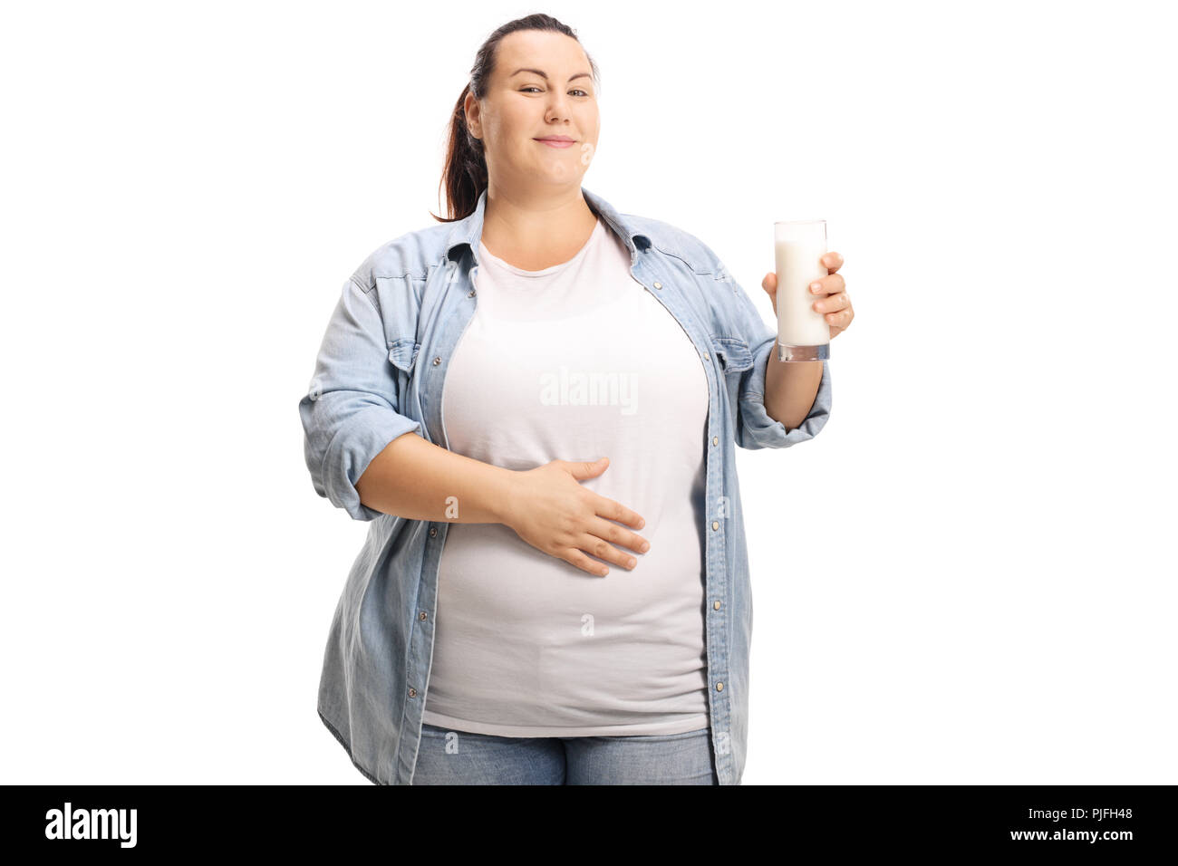 Soddisfatto il sovrappeso donna con un bicchiere di latte tenendo la mano sul suo stomaco isolato su sfondo bianco Foto Stock