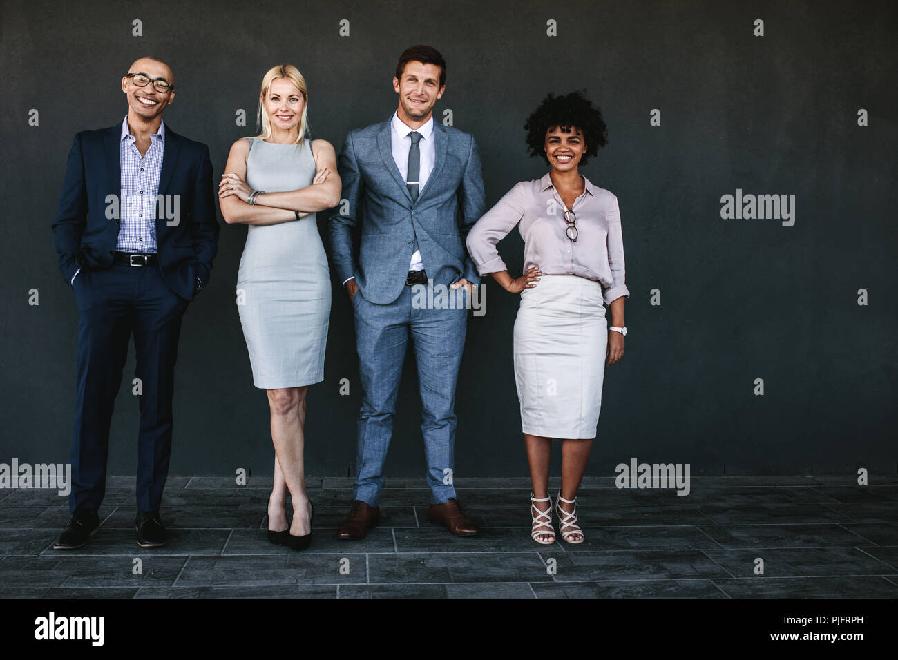 A piena lunghezza Ritratto di business di successo di squadra in piedi insieme e sorridente. Diverse persone di affari in posa per una fotografia contro la parete scura. Foto Stock