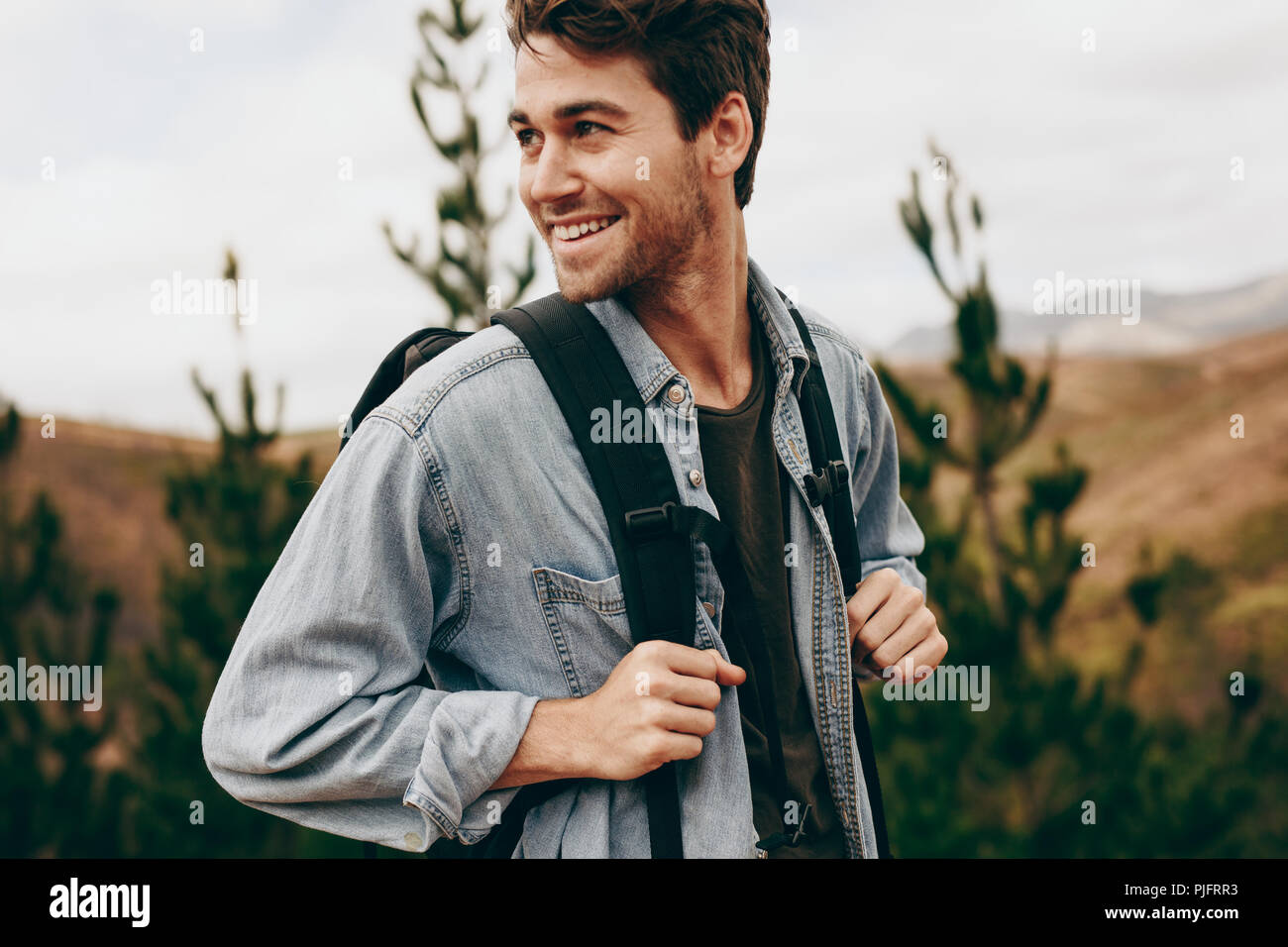 Uomo che cammina attraverso una foresta che indossa una giacca e zaino. Uomo felice su una vacanza escursioni in una località di campagna. Foto Stock