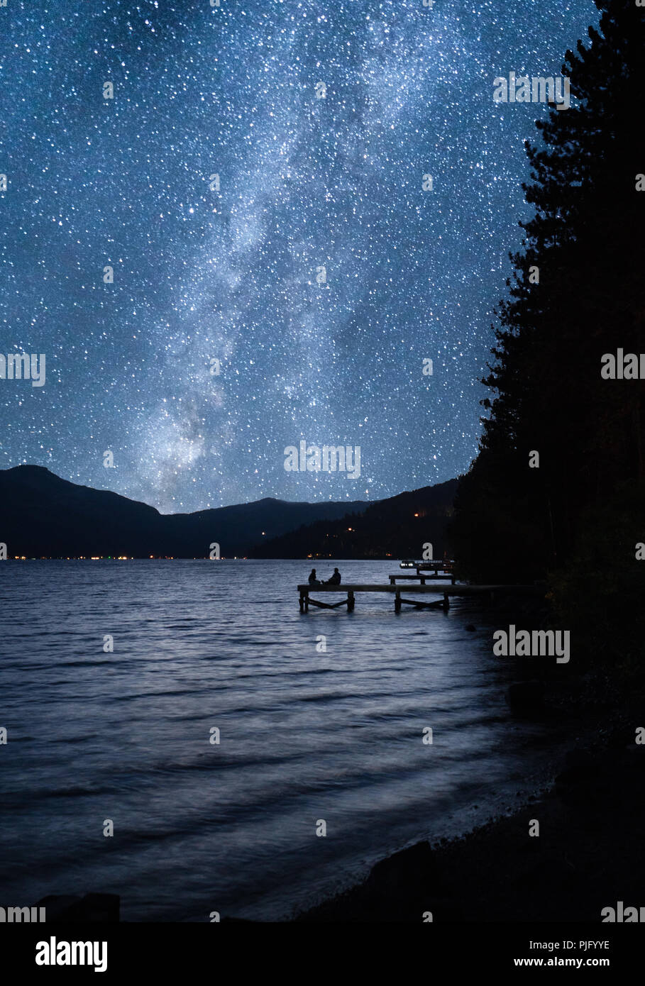 Due persone sedute sul dock con cielo stellato via lattea Foto Stock