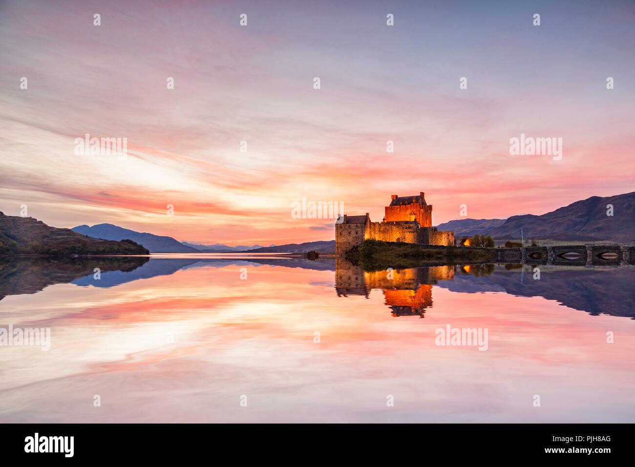 Eilean Donan Castle accesa al crepuscolo, Highland, Scozia, riflesso nelle acque di Loch Duich. Foto Stock