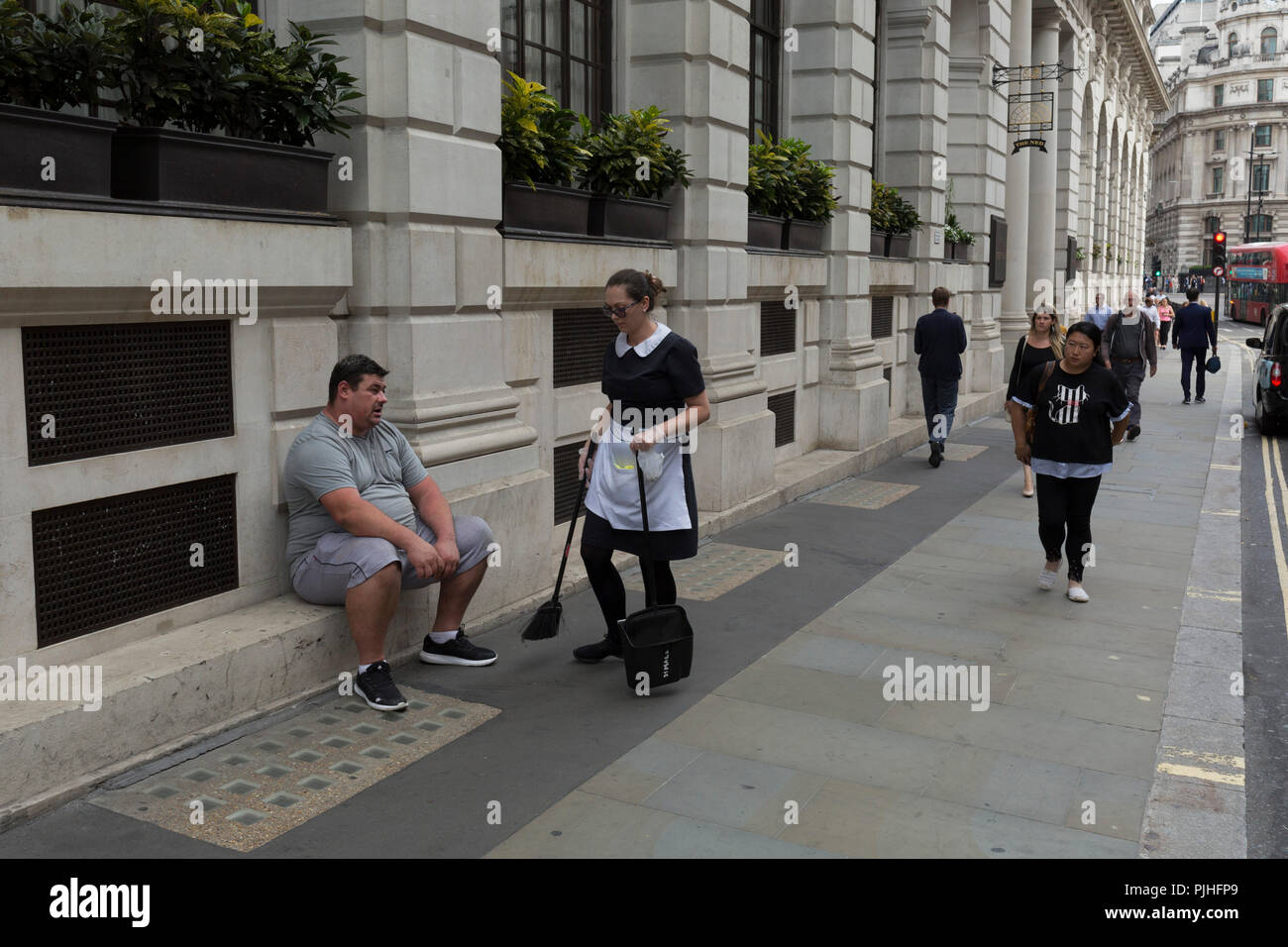 Un dipendente di sesso femminile spazia fino figliata da intorno ai piedi  di un uomo sovrappeso seduti fuori la Ned Hotel nel pollame (street) nella  città di Londra - la capitale del