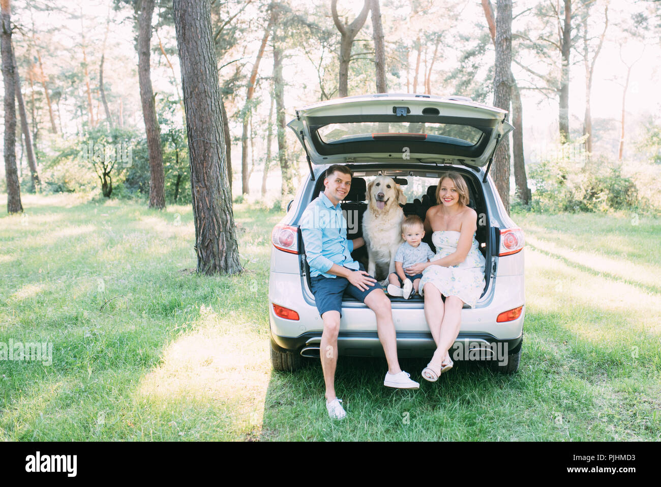Un simpatico giovane famiglia ha divertimento nei boschi mentre è seduto nel bagagliaio della vettura Foto Stock