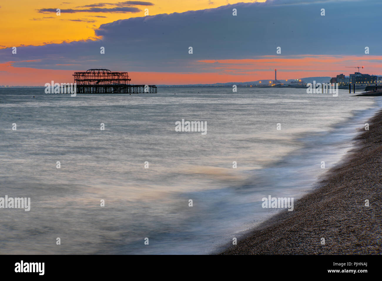 La spiaggia di Brighton, Inghilterra, dopo il tramonto con la rovina del vecchio molo nel retro Foto Stock