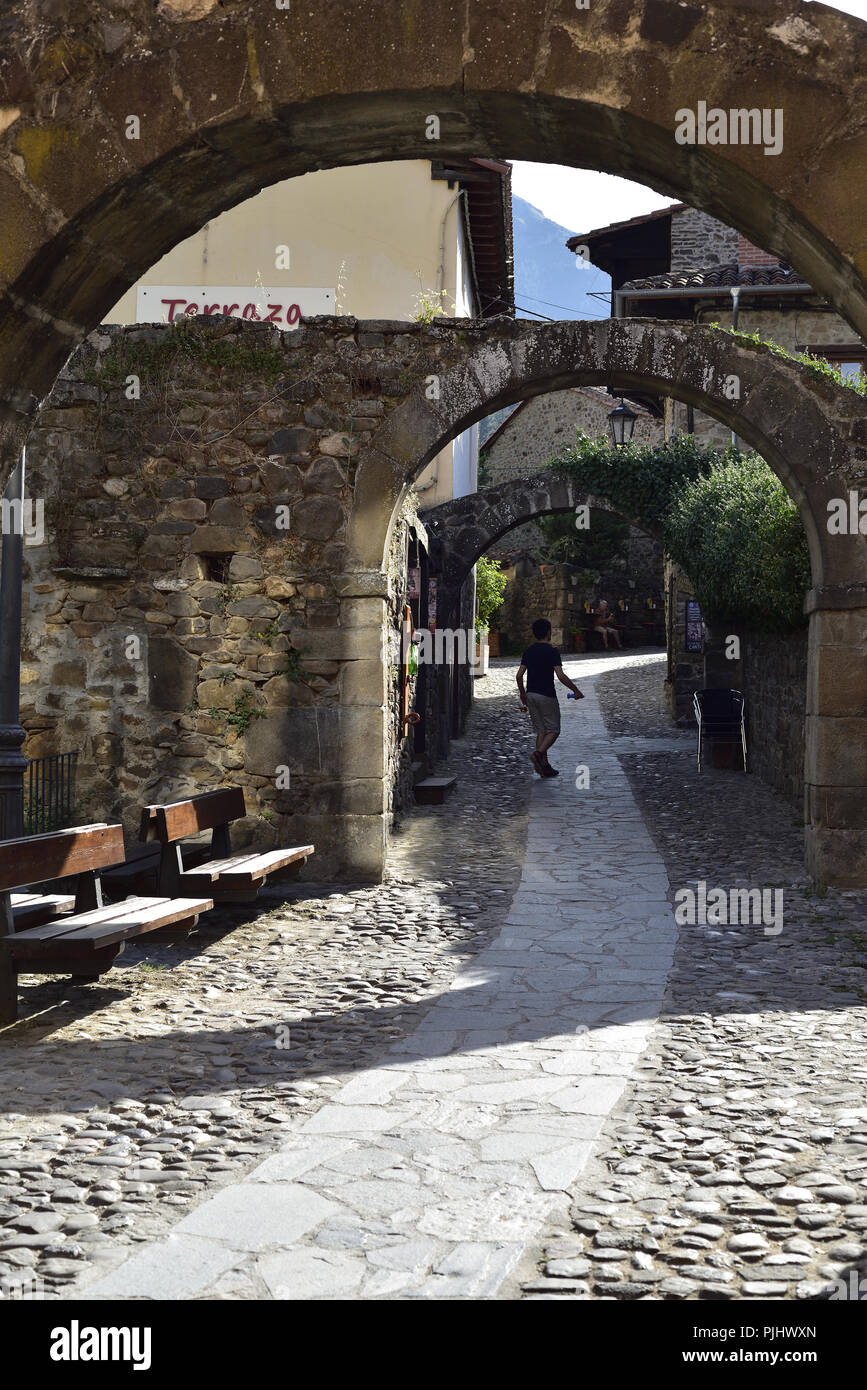 Un tranquillo percorso/road a Potes, Cantabria, Spagna settentrionale. Mostra una serie di tre archi e un ersone walking away fro la fotocamera. Foto Stock