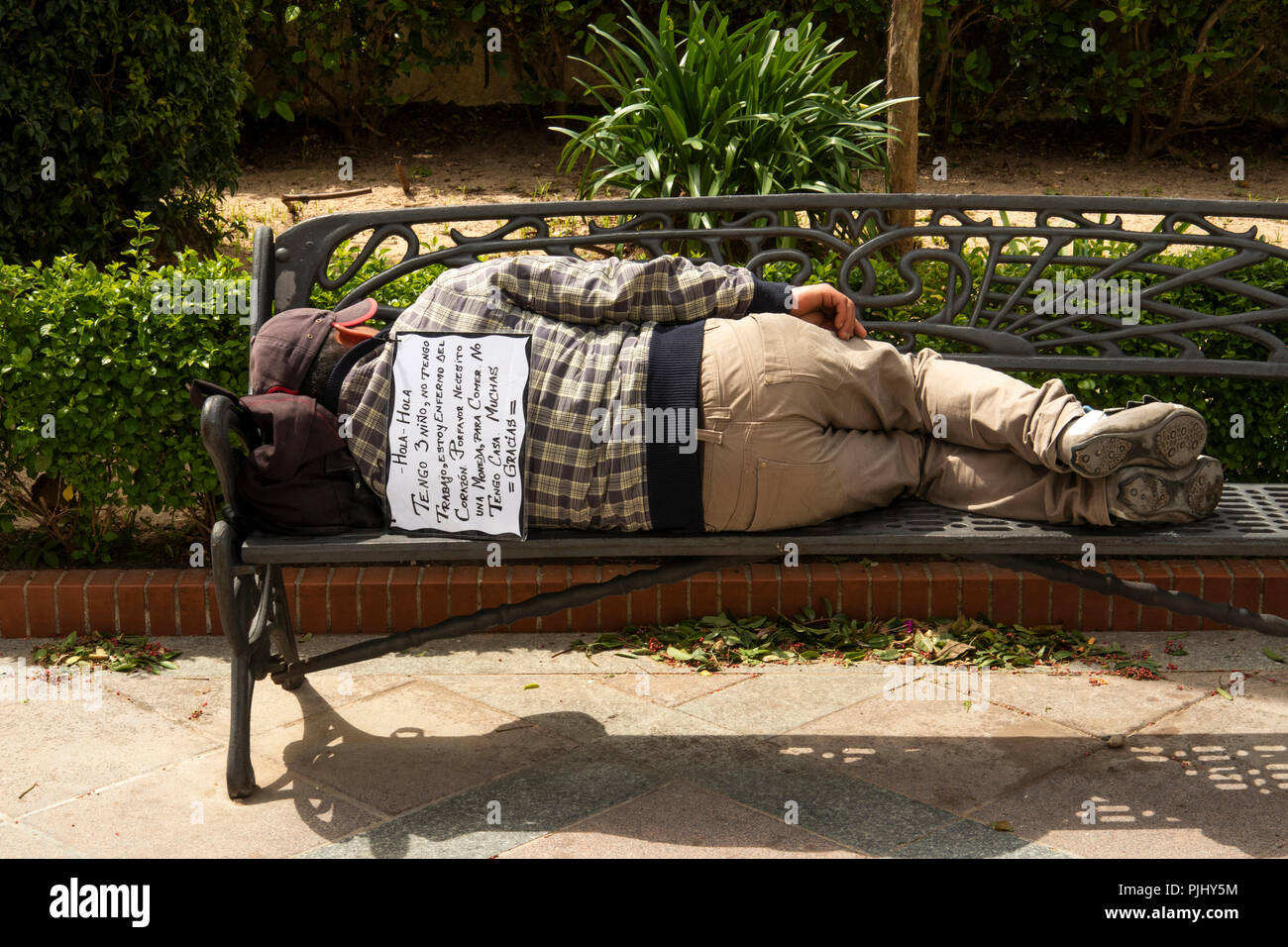 La Spagna, a Jerez de la Frontera, Plaza de Abastos, senzatetto uomo dorme sul banco, con segno di accattonaggio sul retro Foto Stock