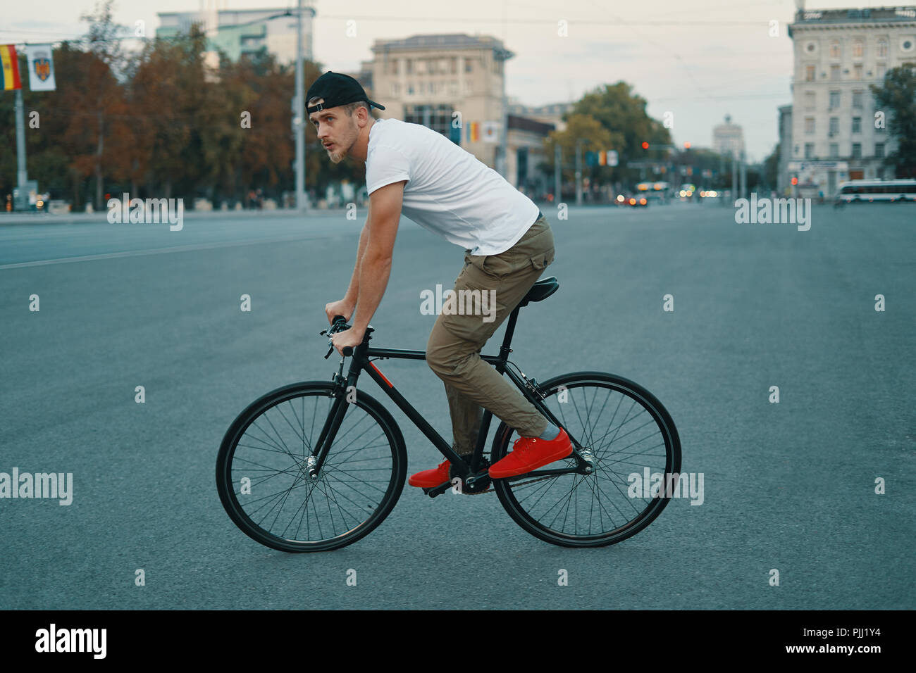 Vista laterale giovane uomo moderno ciclismo su un classico moto sulla strada della città. Copia dello spazio. Attivo e stile di vita ecologico concetto Foto Stock