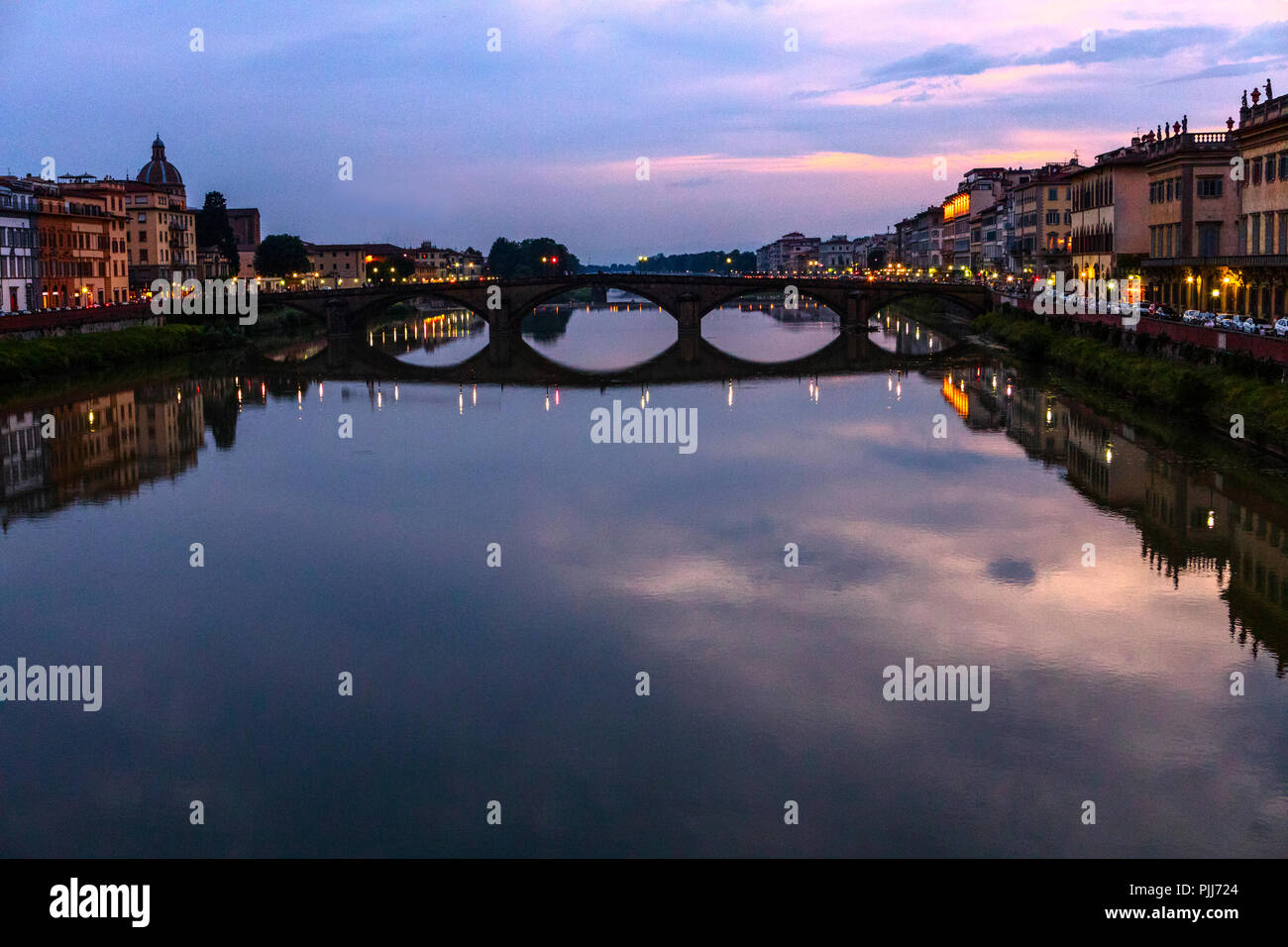 Il Ponte alla Carraia attraversa il fiume Arno nella città di Firenze. Qui il cielo drammatico, di riflessione e di quiete al tramonto è catturato. Foto Stock