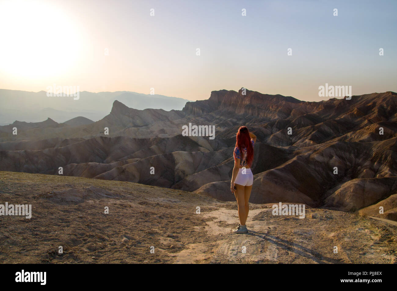 Caldo sole splende in giù prima del tramonto al deserto paesaggio surreale con bella ragazza in piedi dal retro, mistico sognante vista panoramica Zabriskie Point Foto Stock