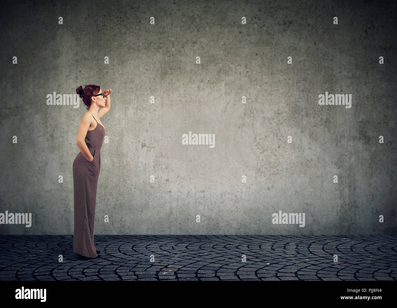 Vista laterale di eleganti donna che guarda lontano in futuro fare previsioni in piedi su sfondo grigio Foto Stock
