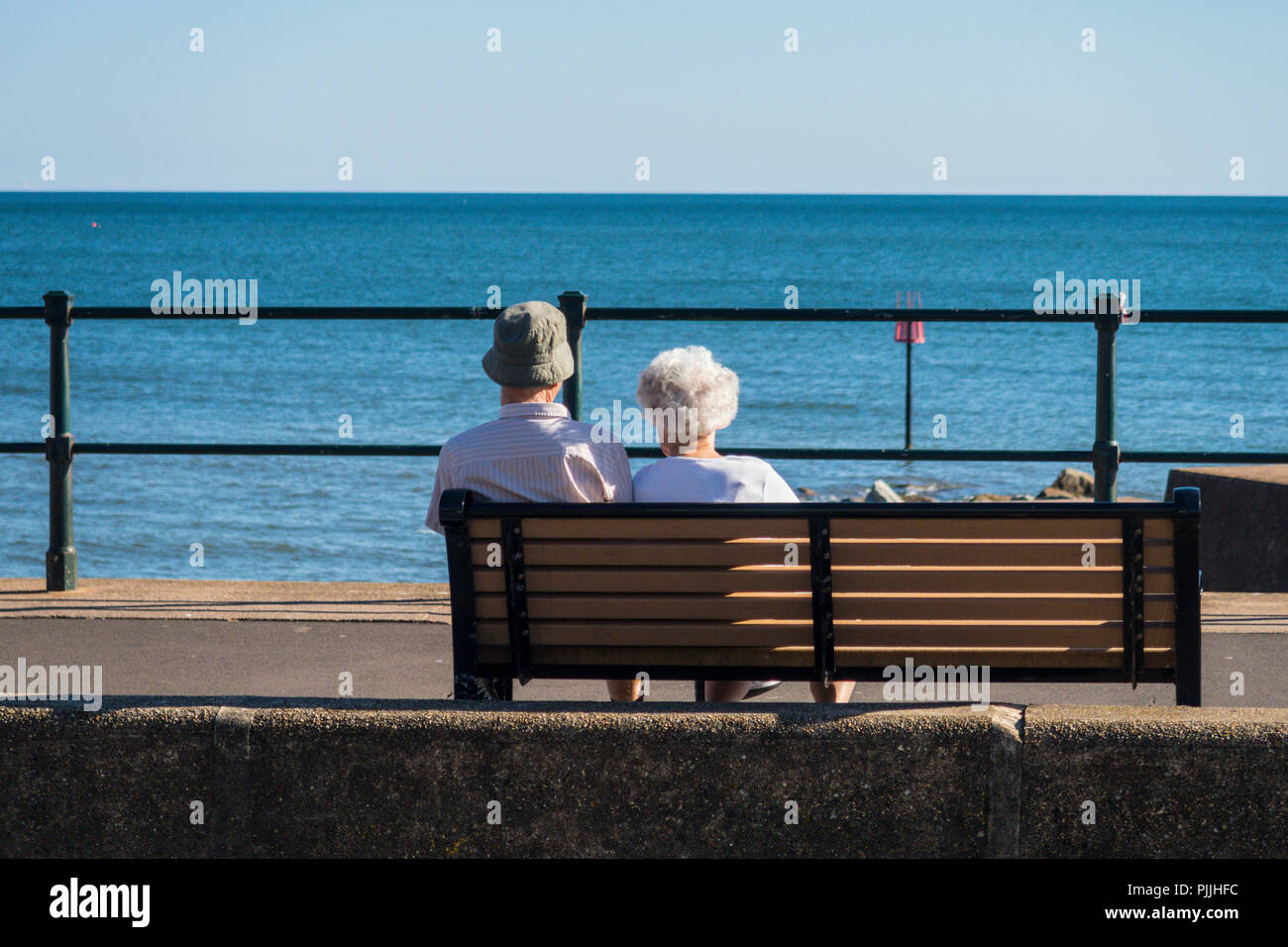 Una coppia di anziani guarda verso il mare da una panca sulla spianata a Sidmouth, nel Devon. Foto Stock