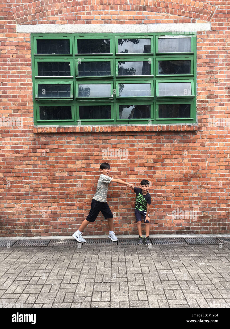 Due fratelli che pongono di fronte a un muro di mattoni in Hong Kong Foto Stock