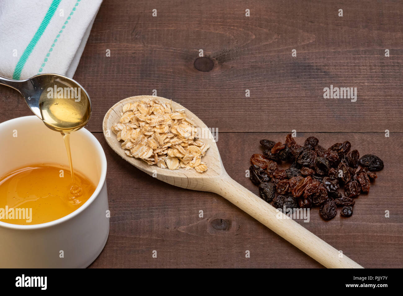 Il cucchiaio di legno laminato con il porridge di avena su uno sfondo di legno, con uvetta e miele. Foto Stock