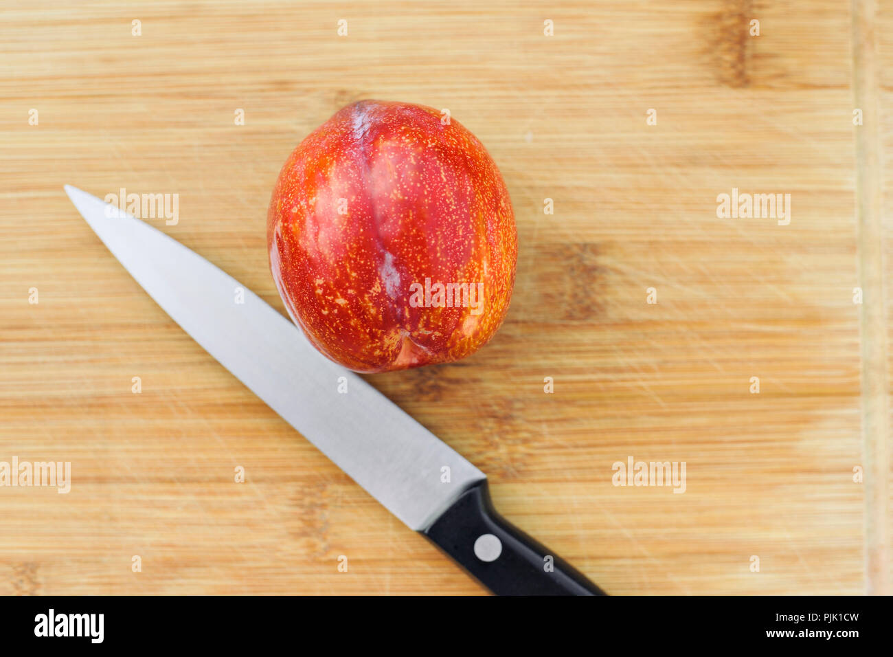 Un coltello fissa accanto a un amigo pluot frutto su un legno tagliere Foto Stock