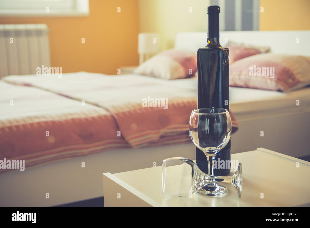 Bottiglia di vino rosso e due bicchieri sul comodino accanto al letto  matrimoniale in hotel moderno