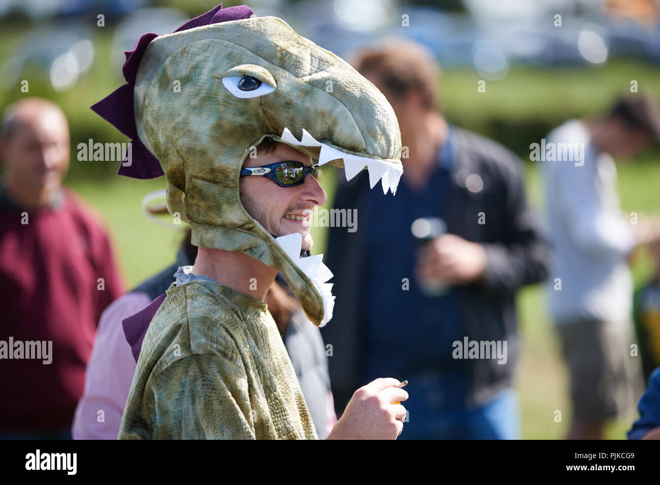 Vista laterale dell'uomo in un dinosauro indossando costumi subglasses in pianura giochi, Thorney, Somerset, Inghilterra Foto Stock