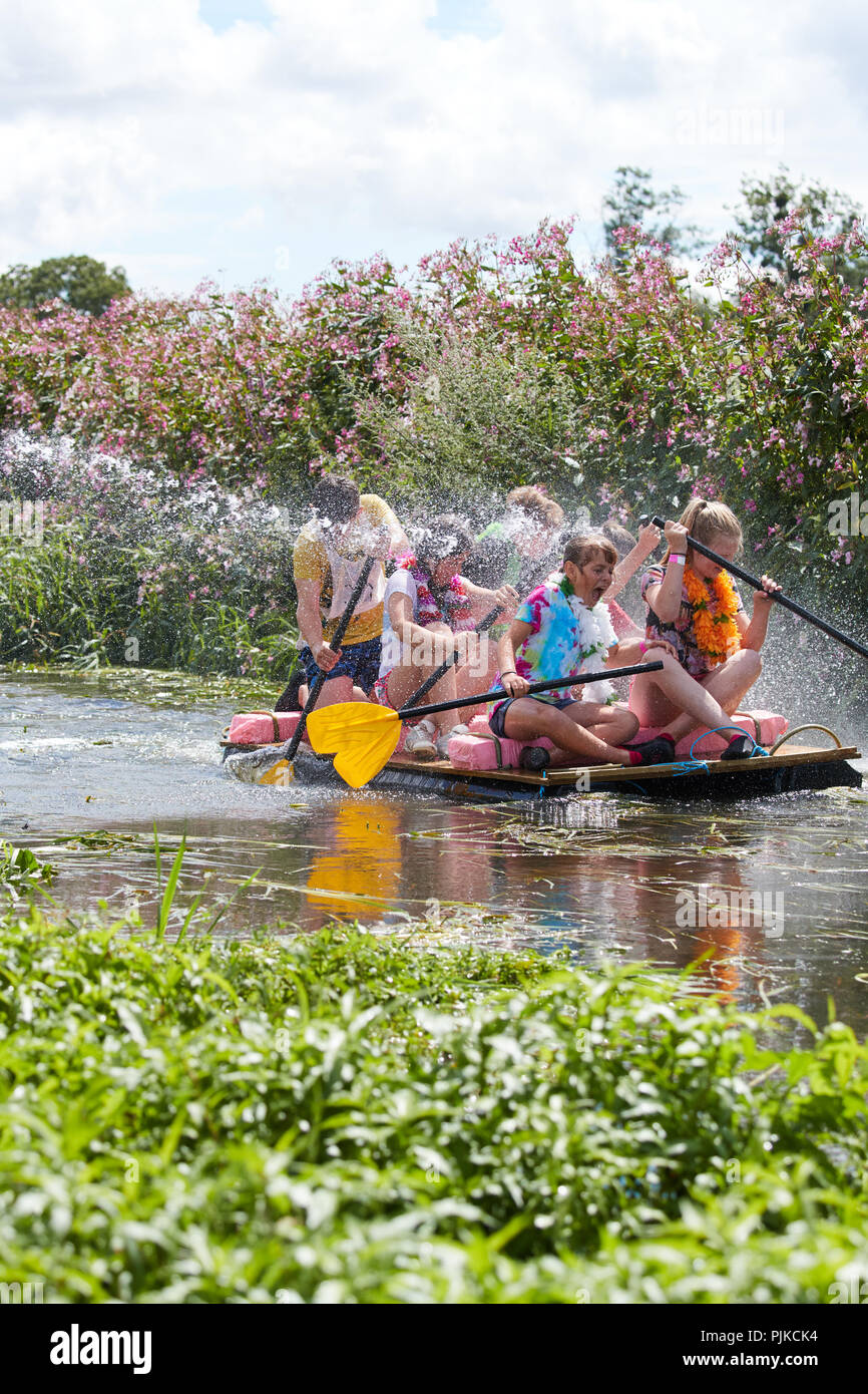 Le giovani ragazze in costumi hawaiano canottaggio una zattera lungo un fiume e bagnare a Pianura Giochi, Thorney, Somerset, Inghilterra Foto Stock