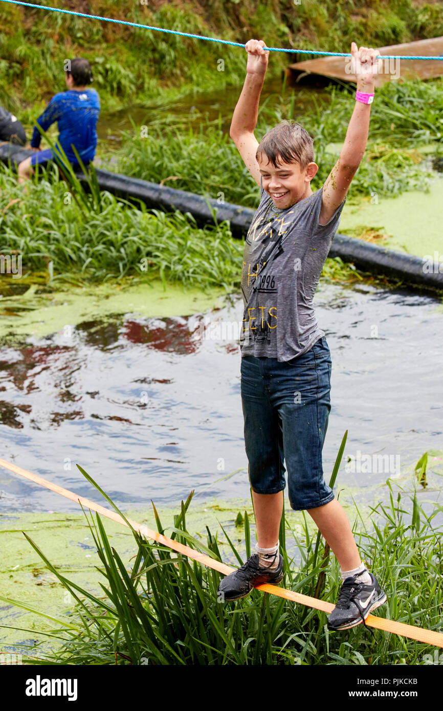 Un wet giovane ragazzo camminando lungo una linea di lasco su un ostacolo di acqua in corso presso la pianura giochi, Thorney, Somerset, Inghilterra Foto Stock