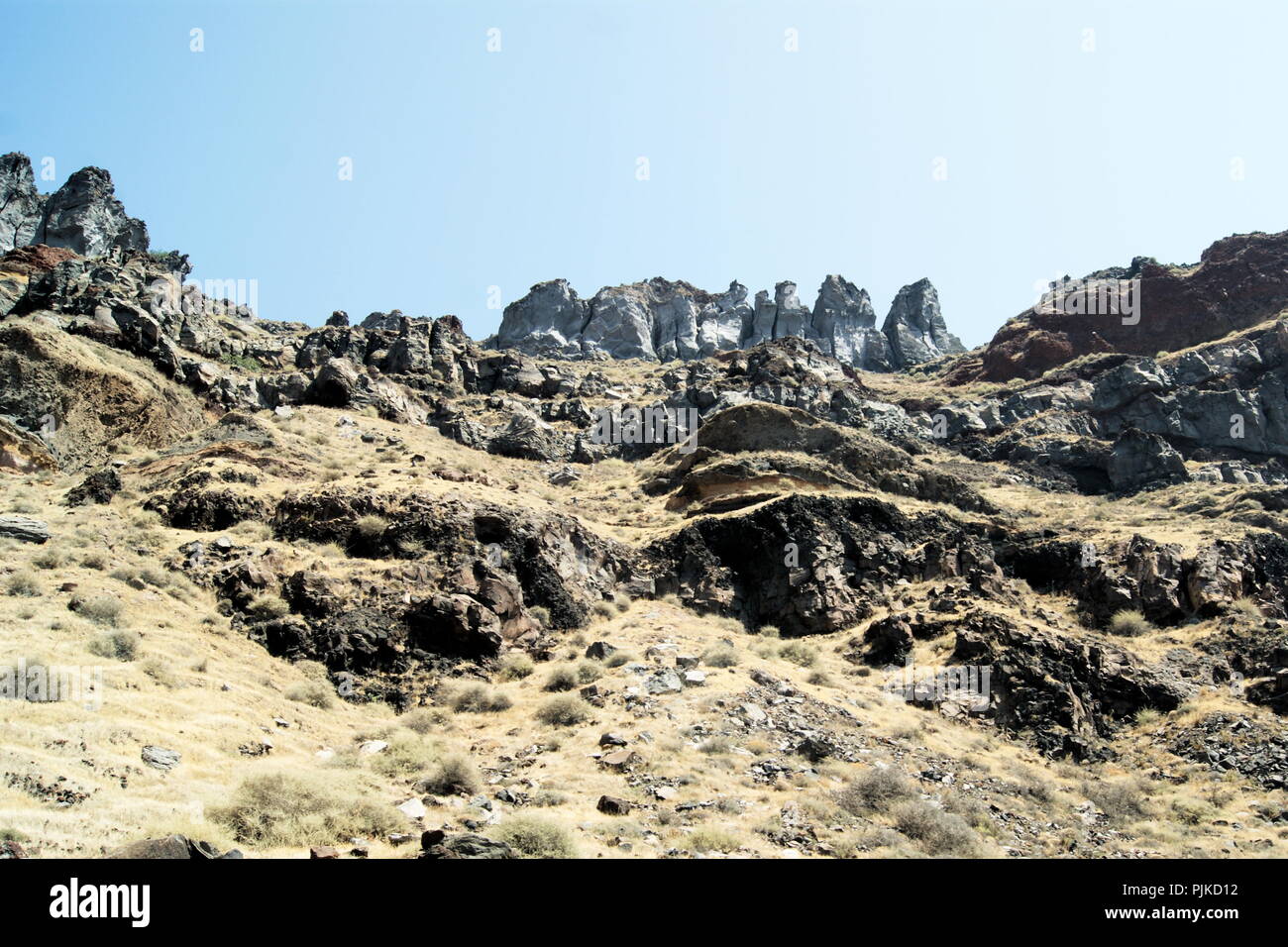 Grecia, l'isola di Thirasia. Suggestive formazioni rocciose vulcaniche che si innalzano dal mare a picchi frastagliati e drammatici. Cielo blu - spazio di copia. Foto Stock