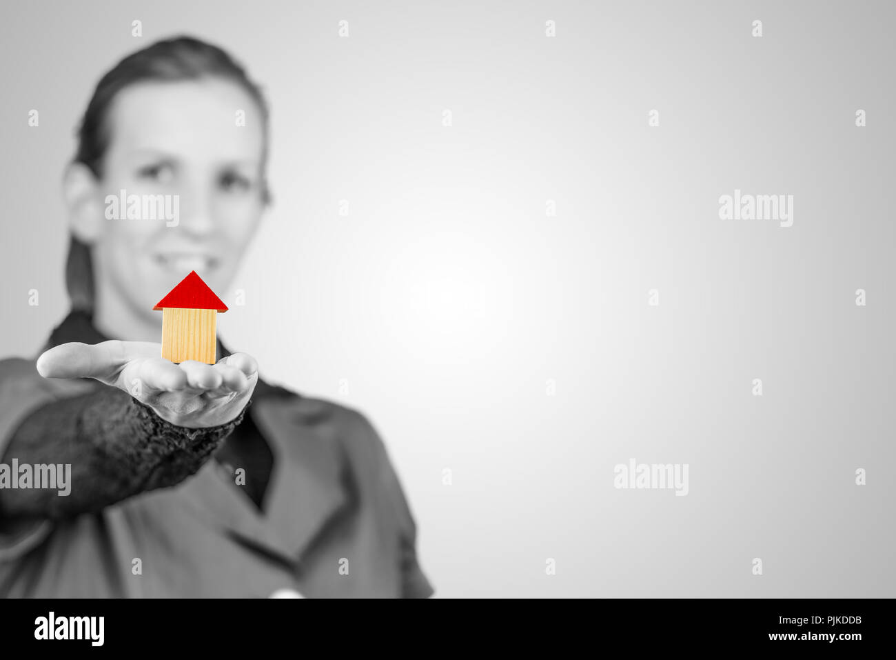 Immagine in scala di grigi con colorazione selettiva di un sorridente giovane donna tenendo fuori un modello di casa sul palmo della sua mano concettuale del gol, proprietà, inv Foto Stock