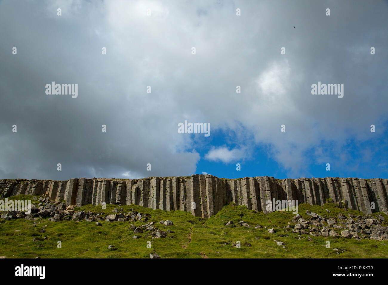 L'Islanda, Snaefellsnes peninsula, Gerðuberg scogliere, colonne di basalto su verde prato, cielo blu con nuvole, Foto Stock